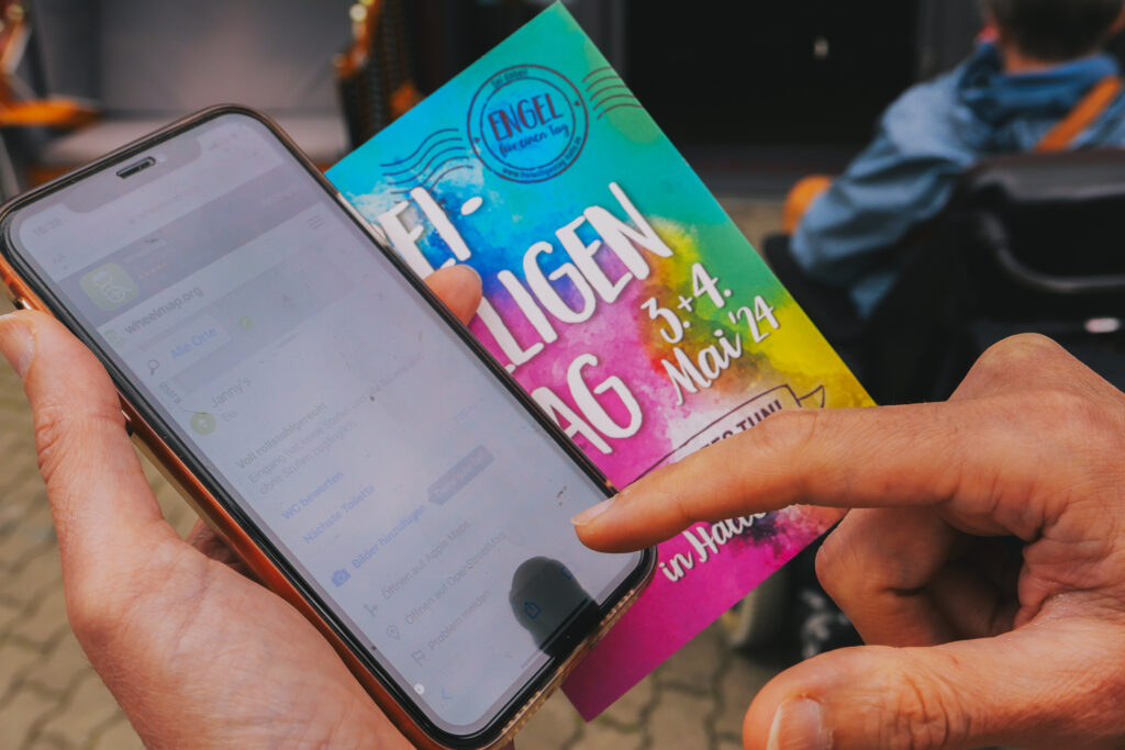 Ein Handy, das in der Hand gehalten wird und auf das gerade getippt wird. Darauf ist die Wheelmap-App geöffnet.